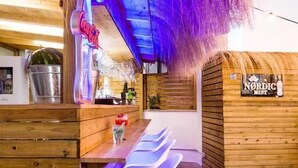 Zona de bar al aire libre con temática nórdica, mobiliario de madera y un letrero de neón.