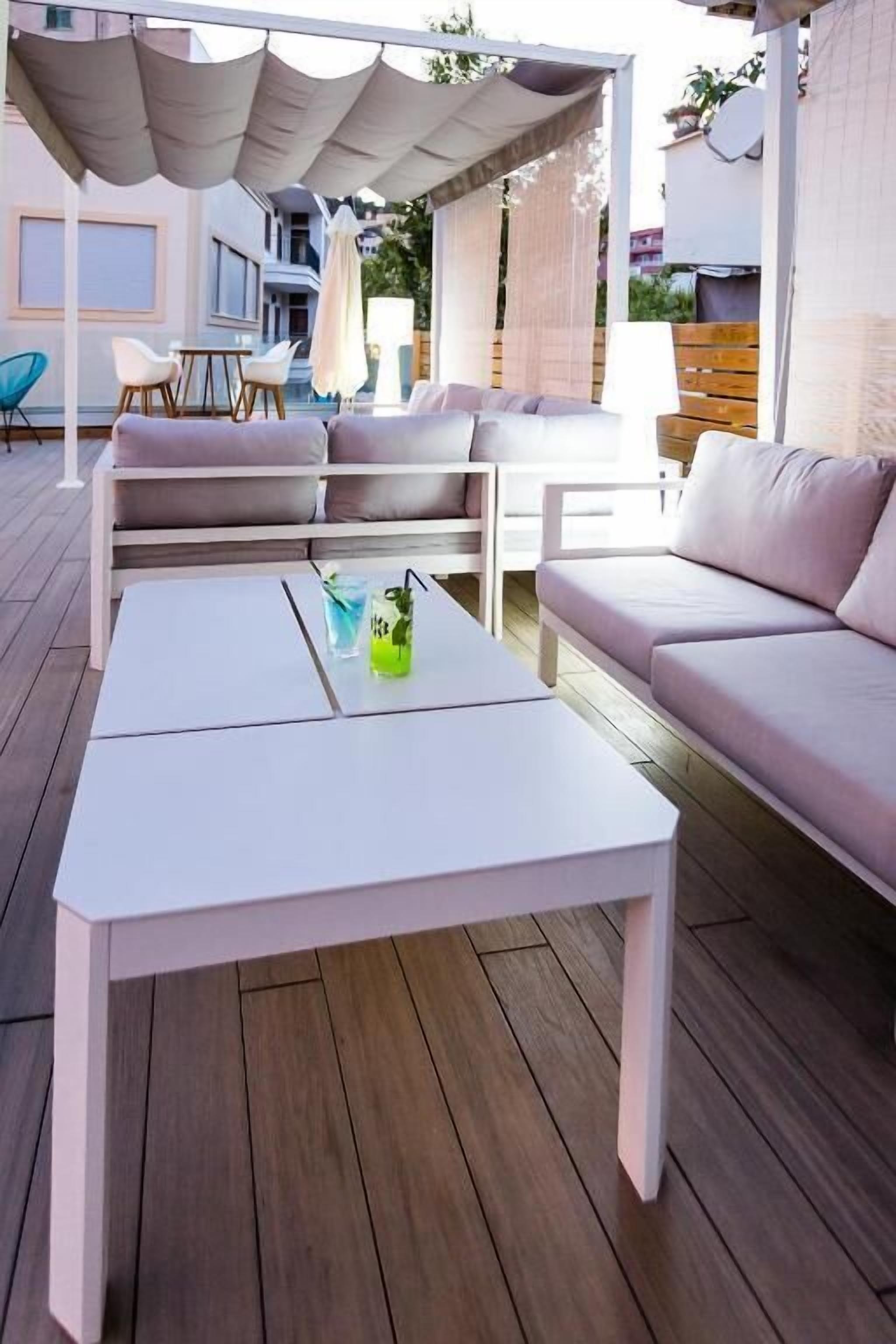 Un espace extérieur aménagé avec une table blanche, des sièges rembourrés et un auvent.