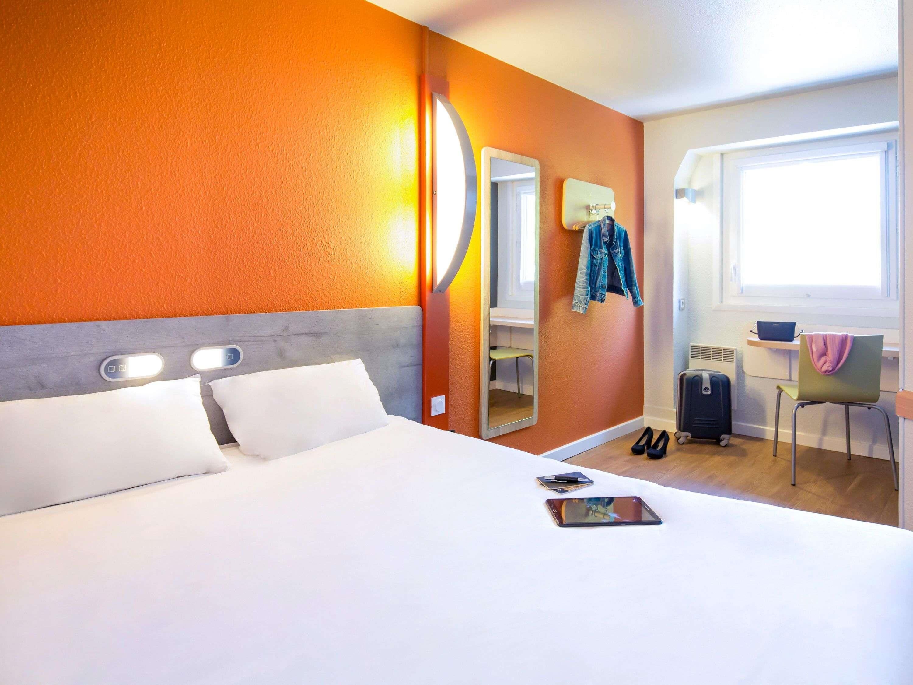 Una habitación de hotel con cama, escritorio, silla, maleta y espejo.