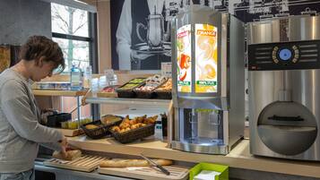 Zona de bufé con diversas opciones de comida, como pan, pastelería y un dispensador de bebidas.