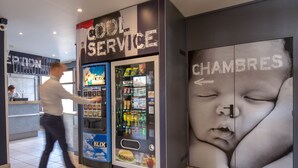 A vending machine with a 'Cool Service' sign, a refrigerator stocked with beverages, and a large wall advertisement featuring a baby's face. - ibis budget Vienne Sud (Vienne)