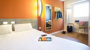 A hotel room with a bed, a bedside table, a mirror, a window, and a chair. - ibis budget Vienne Sud (Vienne)