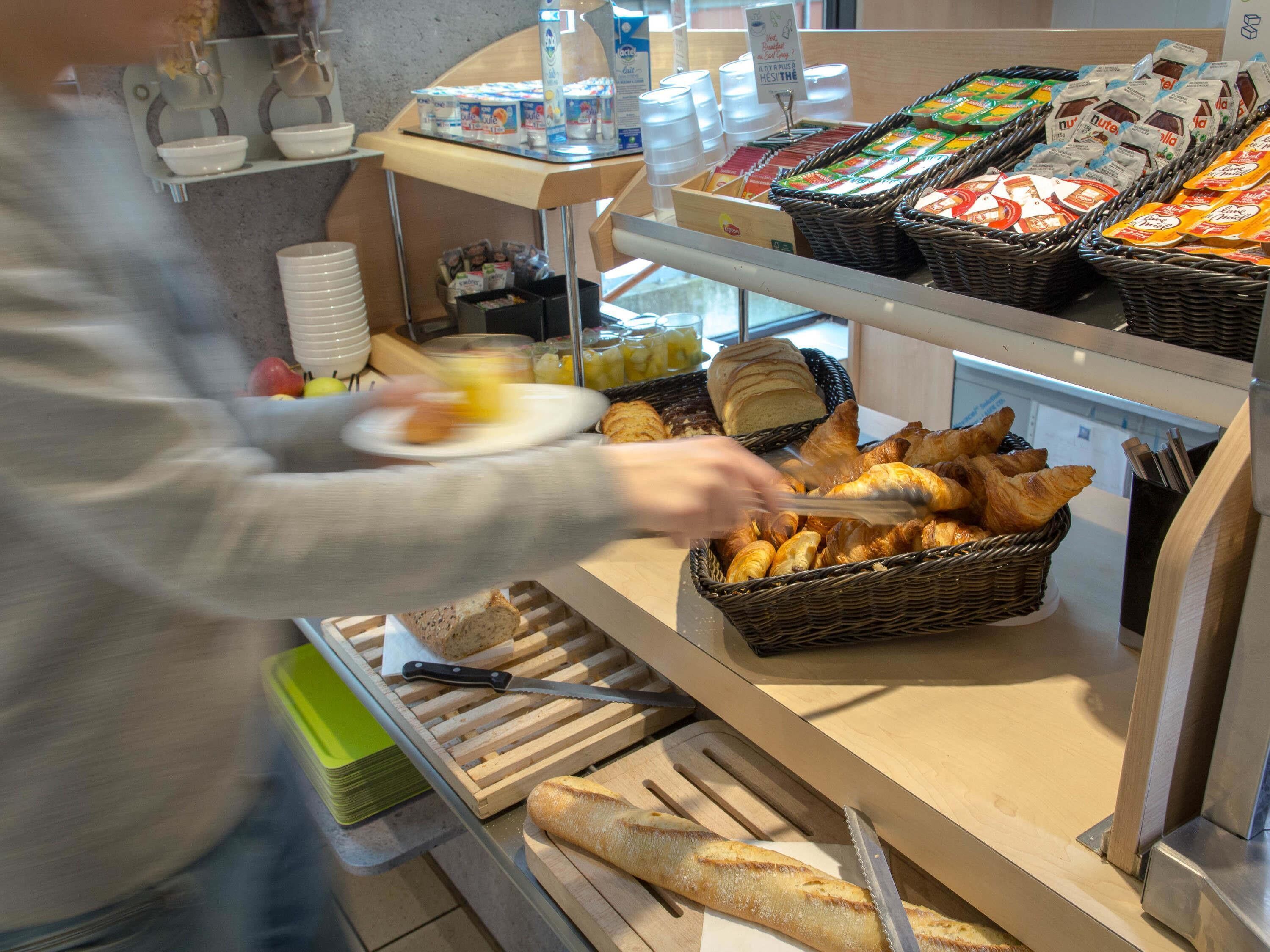 A buffet counter with various food items, including bread, pastries, and condiments.