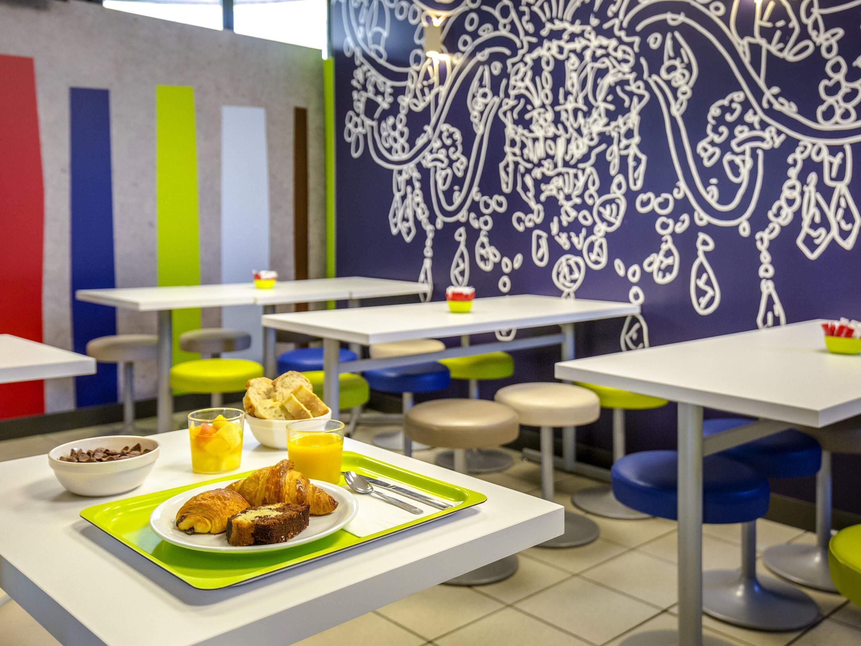 Un comedor con mesas y sillas, una bandeja con comida y bebidas, y una pared con un diseño decorativo.