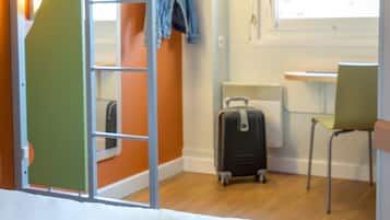 Une chambre d’hôtel avec un lit superposé, un bureau, une chaise, une valise et une fenêtre donnant sur un paysage agréable.