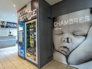 A hotel reception area with a vending machine, a reception desk, and a wall with a large advertisement.