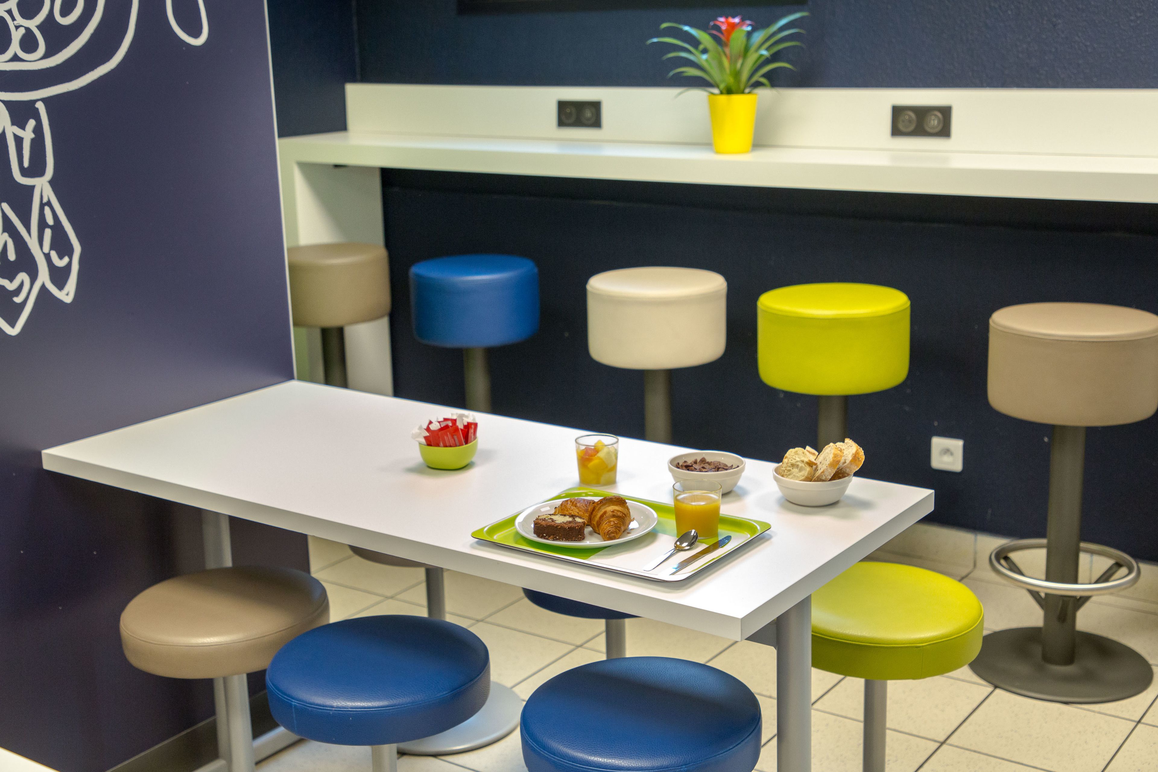 Un coin repas avec une table blanche, plusieurs tabourets et une table dressée pour le petit-déjeuner, comprenant des croissants et du jus d’orange.