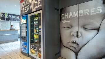 A hotel reception area with a vending machine, a reception desk, and a wall with a large advertisement.
