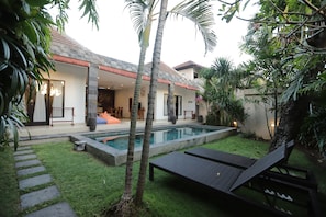 A modern house with a swimming pool, a patio with lounge chairs, and a well-maintained garden.