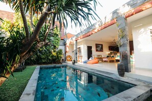 Una piscina rodeada de abundante vegetación y un interior moderno con zona de comedor.