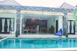 A poolside area with a clear view of the pool, a seating area with a sofa and chairs, and a large painting on the wall.