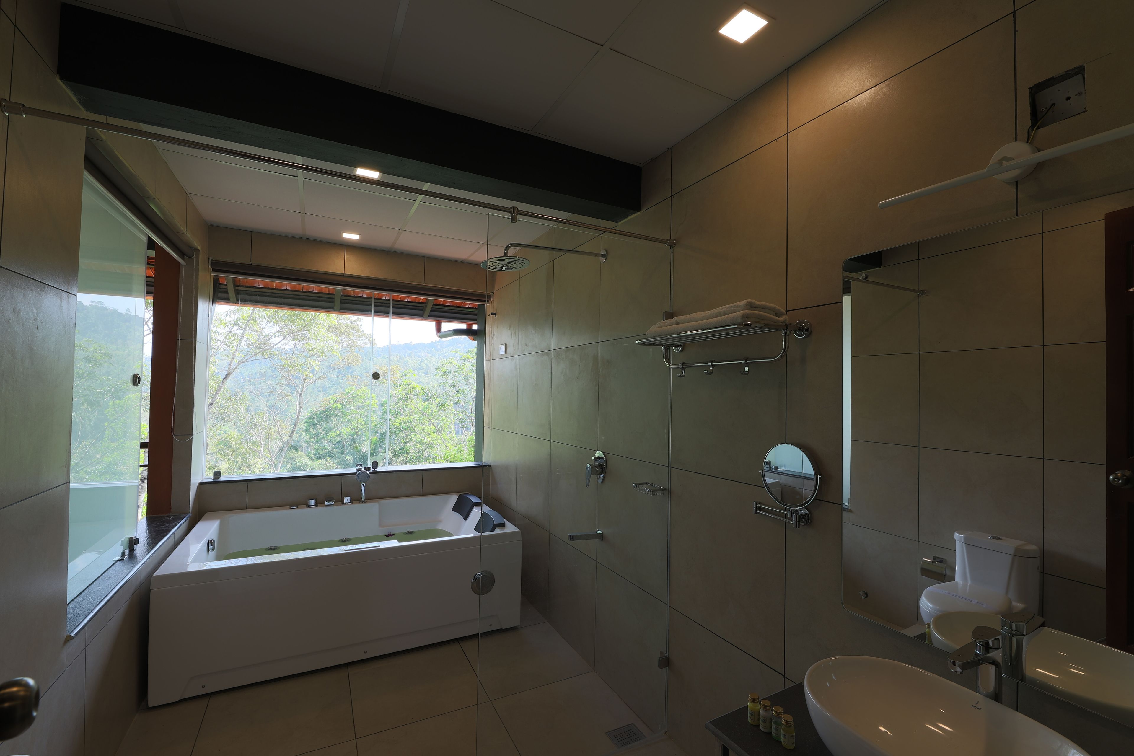 A modern bathroom with a large bathtub, a sink, and a toilet. There is a window providing a view of greenery outside.