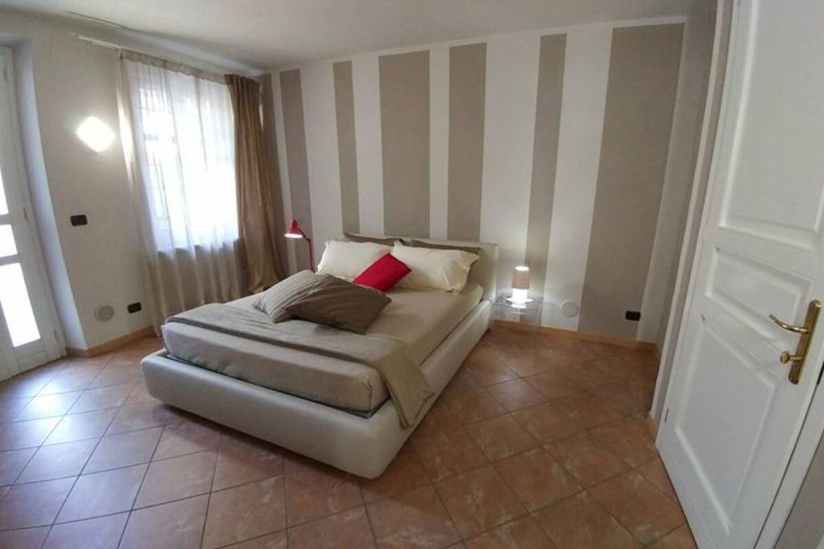 A bedroom with a bed, a bedside table, a lamp, a door, and a window with curtains.
