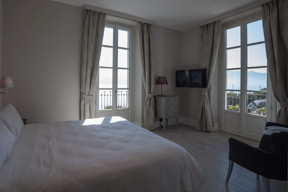 A hotel room with a large bed, a TV, a desk, and a balcony with a view.