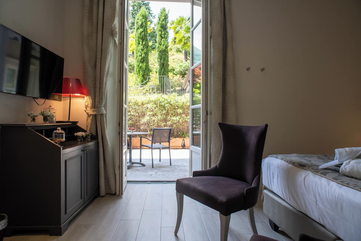 A hotel room with a bed, a chair, a desk with a lamp, and a TV on the wall.