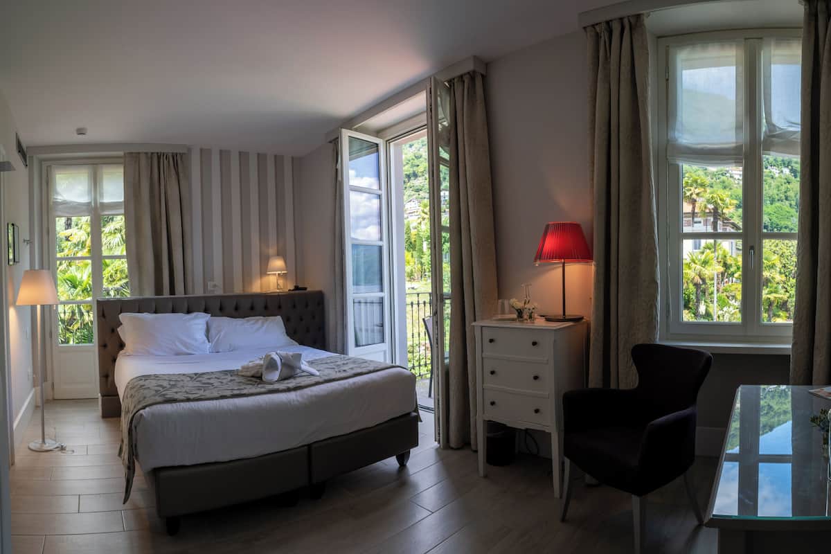 A neatly arranged bedroom with a large bed, bedside tables, a chair, and a view of greenery through the windows.