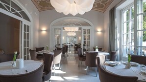 A spacious dining area with high ceilings and elegant chandeliers. Tables are arranged in a symmetrical layout, and the room features large windows allowing natural light to enhance the space. - Park Hotel Italia (Cannero Riviera)