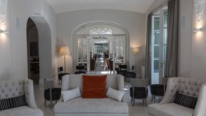 A spacious living room with a central sofa, two armchairs, and a dining area visible through an archway. - Park Hotel Italia (Cannero Riviera)