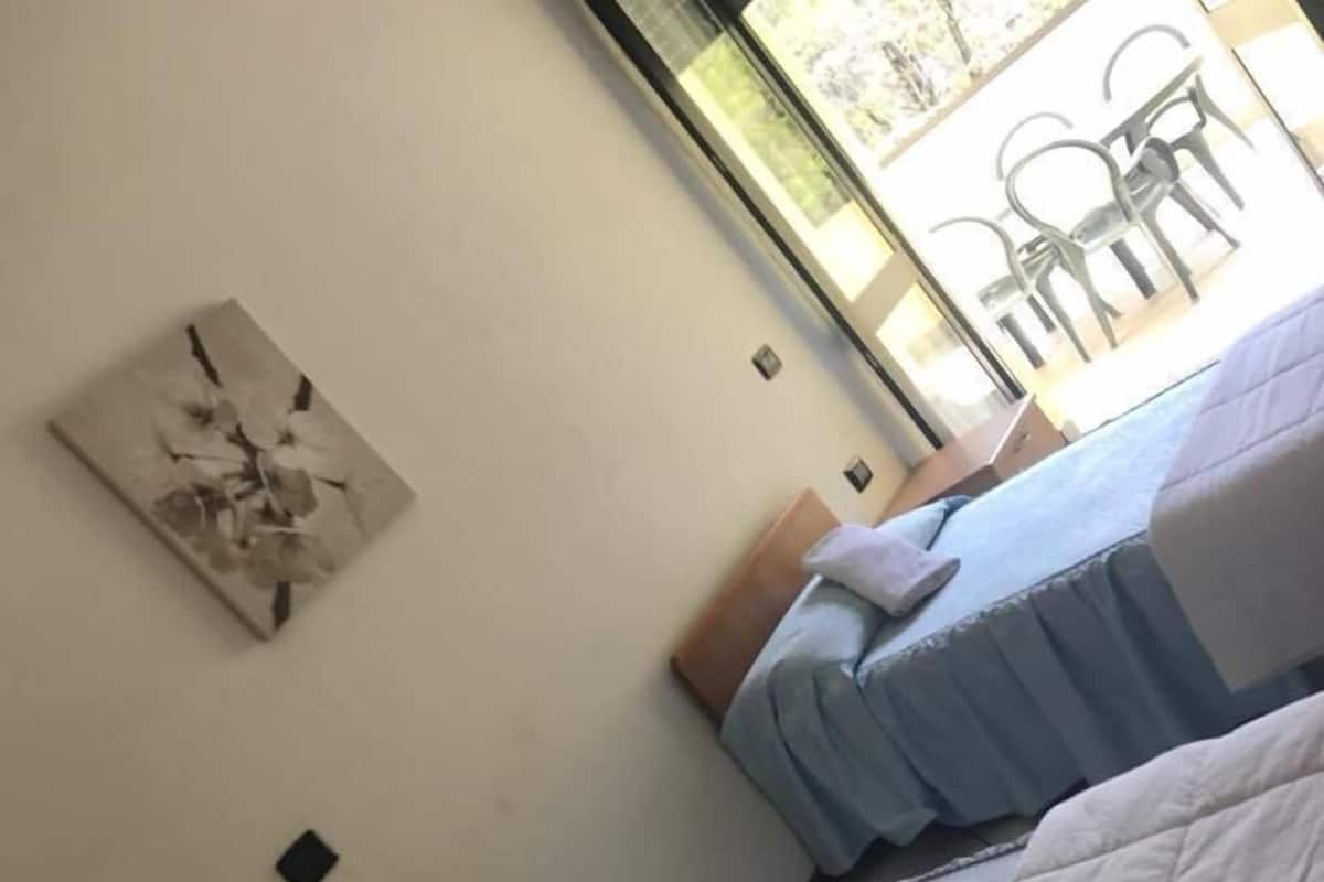 Hotellihuone, jossa on kaksi sänkyä, seinällä taulu ja ikkuna, josta avautuu näkymä ulkona oleviin tuoleihin.