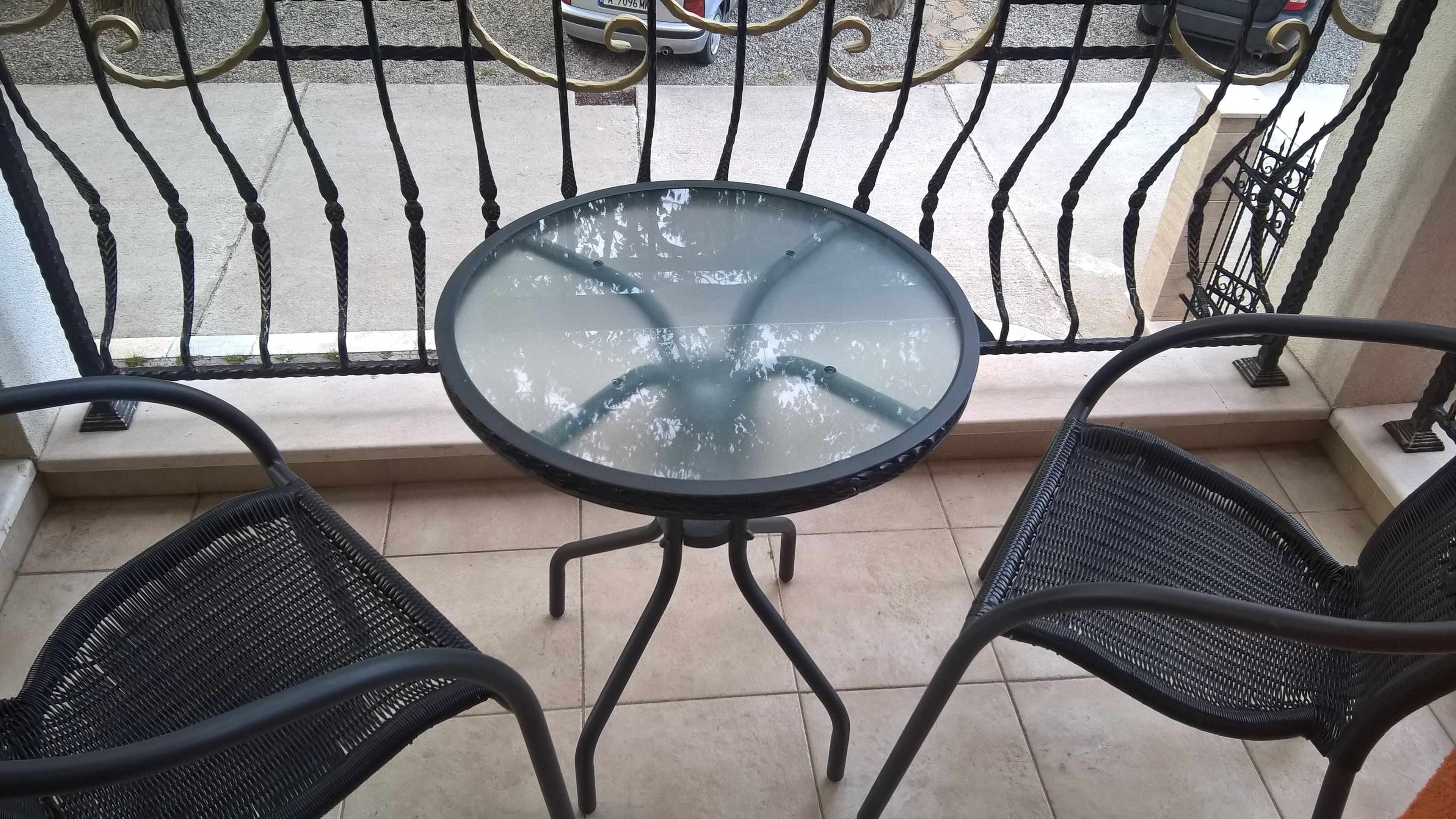 A glass-top table with two black wicker chairs on a balcony with a metal railing.