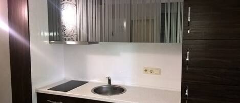 A kitchen with a stainless steel sink, a black countertop, and a white backsplash.