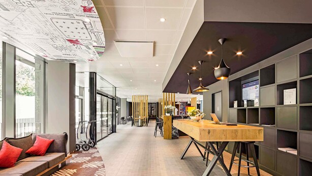 A modern hotel lobby with a long reception desk, seating area, and a large window providing a view of the outdoors.