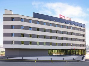 Ein mehrgeschossiges Hotel mit modernem Design, das durch ein Flachdach, große Fenster und eine gut sichtbare Beschilderung für das ibis Hotel gekennzeichnet ist.