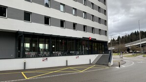 Ein modernes Gebäude mit flacher Fassade, großen Fenstern und einer überdachten Außenbereich-Sitzgelegenheit.