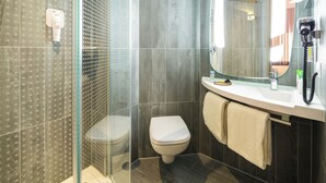 Ein modernes Badezimmer mit Duschkabine aus Glas, Toilette, Waschbecken mit Spiegel und einem Fön auf der Ablagefläche.