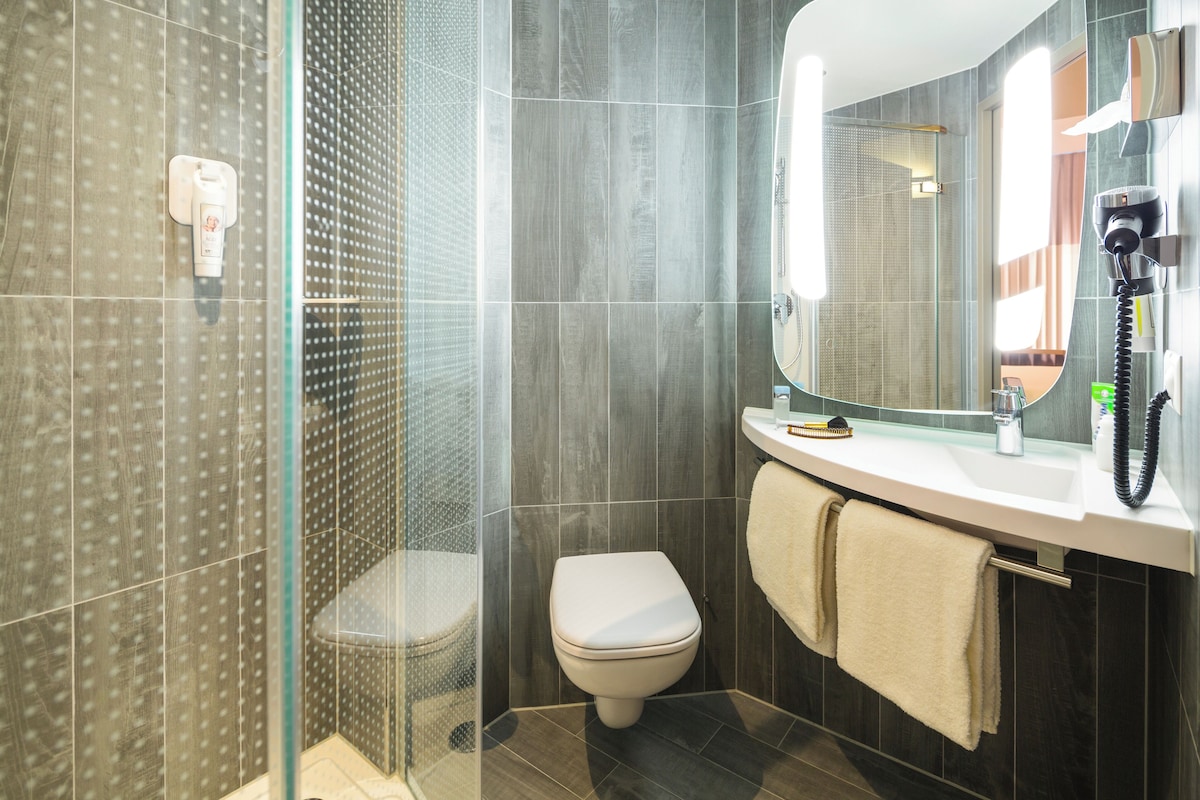 Une salle de bain moderne avec une douche à parois de verre, des toilettes, un lavabo avec un miroir et un sèche-cheveux posé sur le comptoir.