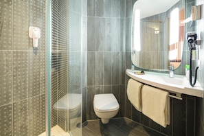 Une salle de bain moderne avec une douche à parois de verre, des toilettes, un lavabo avec un miroir et un sèche-cheveux posé sur le comptoir.