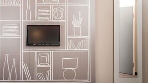 A wall with a flat-screen TV mounted above a chalkboard-style wall art depicting various objects like books, a radio, and a clock.