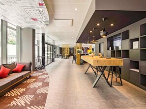 Een moderne hotelentree met een lange receptiebalie, een zithoek en een groot raam met uitzicht op de omgeving.