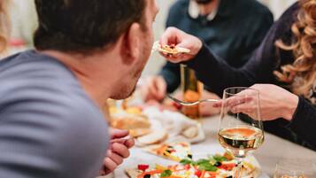 Eine Gruppe von Menschen isst Pizza an einem Tisch, ein Weinglas steht daneben.