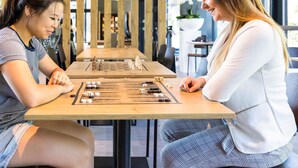 Two people playing a board game at a wooden table in a modern indoor setting.