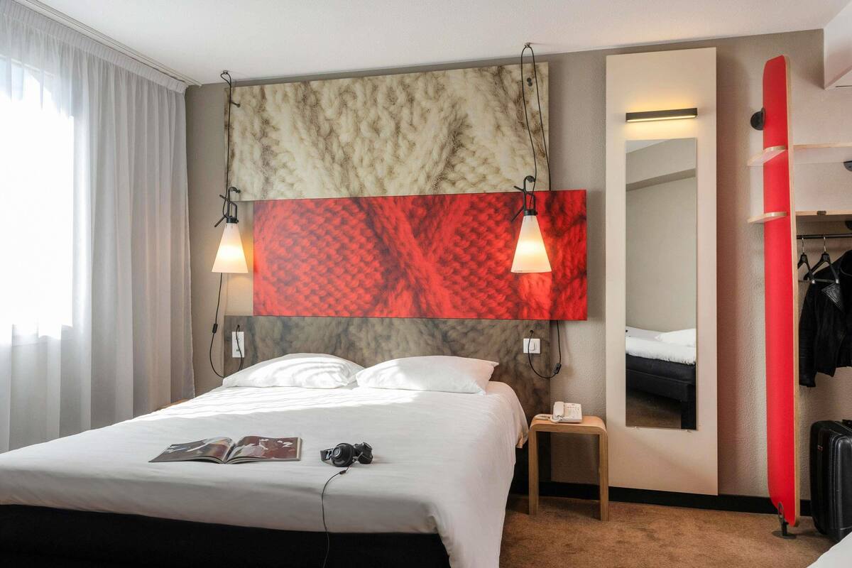 Une chambre d’hôtel avec un lit, une table de chevet, une lampe et un miroir.