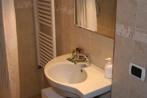 Un baño con lavamanos blanco, espejo y toallero.