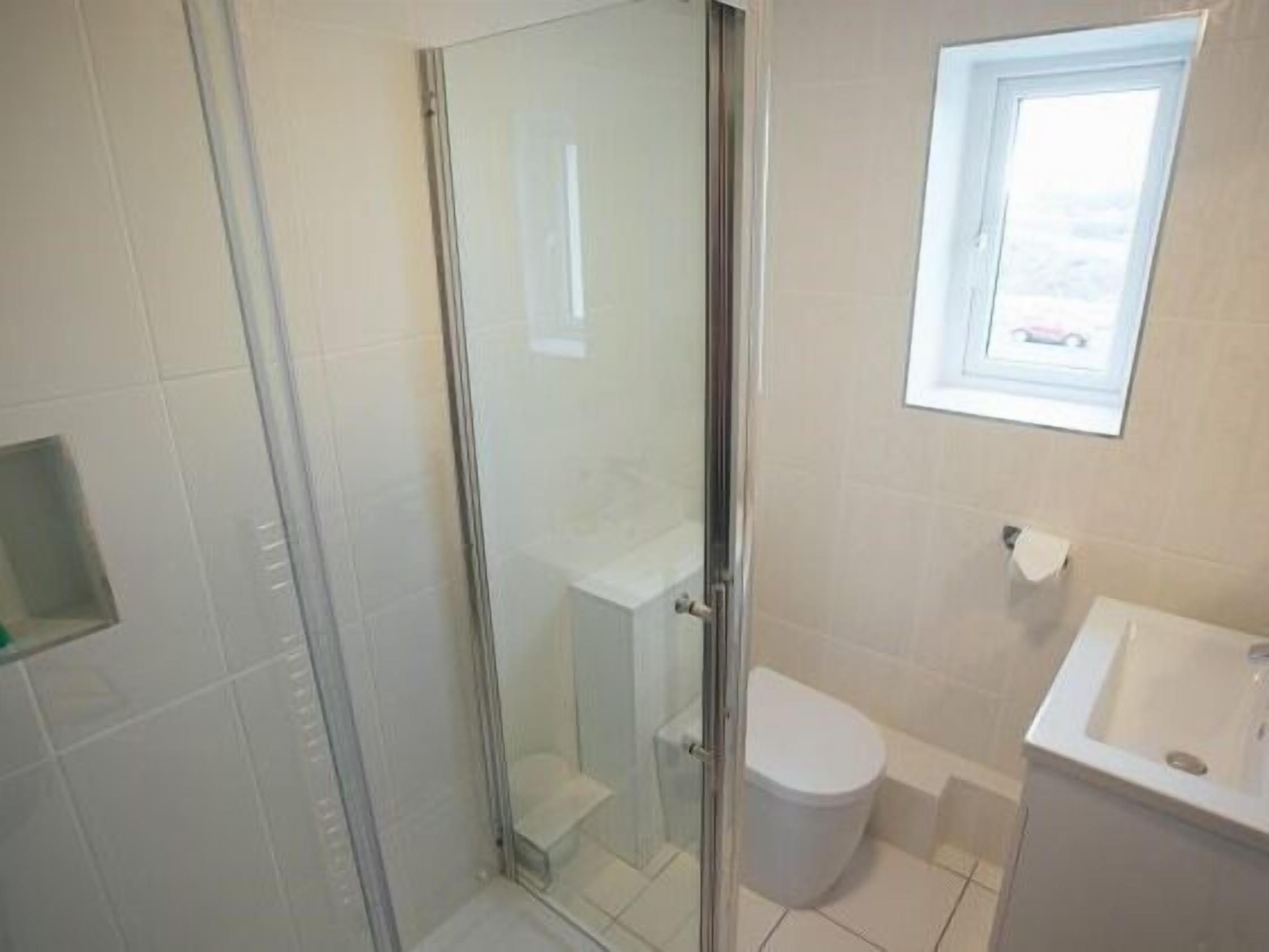 A bathroom with a glass shower enclosure, a toilet, and a sink.