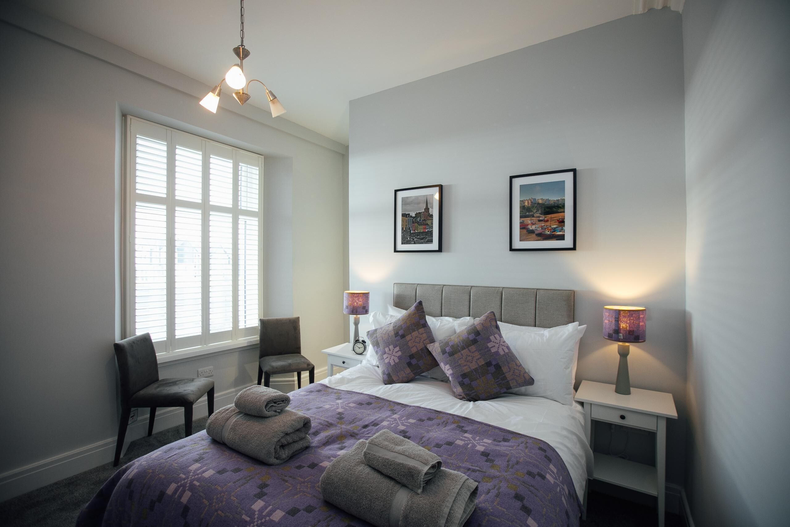 A neatly arranged bedroom with a large bed, two bedside tables, a chair, and a window with blinds.