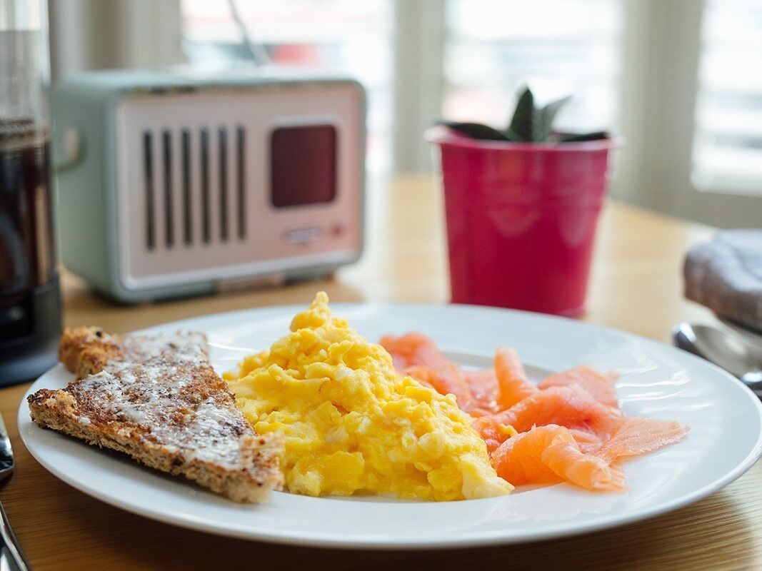 A plate with scrambled eggs, smoked salmon, and toast on a table with a radio and a potted plant in the background.