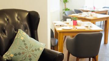 Un sofá de cuero con un cojín estampado, una mesa de comedor con sillas y una planta al fondo.