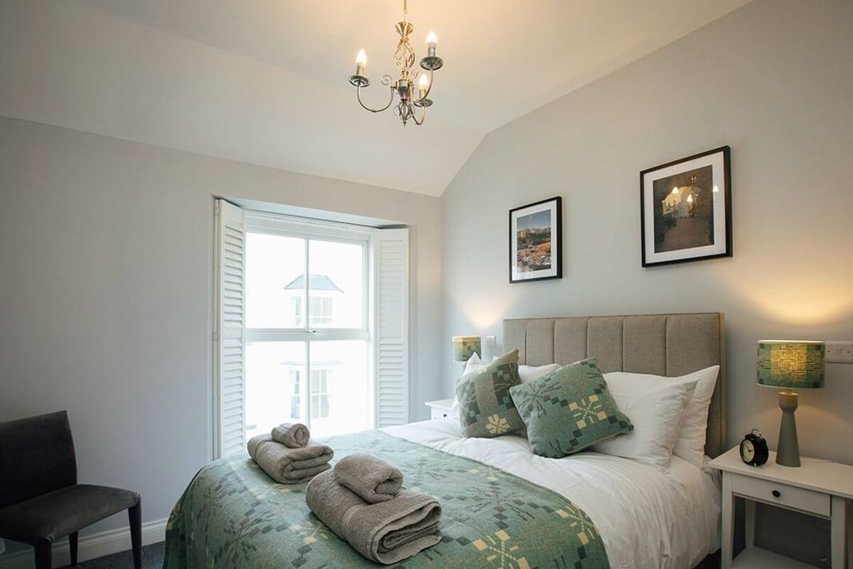 Une chambre à coucher avec un lit, deux tables de chevet, une chaise, une fenêtre et un lustre.