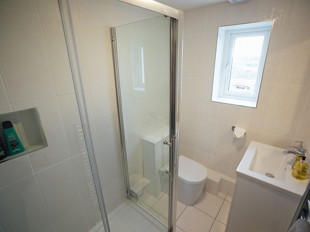 A bathroom with a glass shower enclosure, a toilet, a sink, and a window.