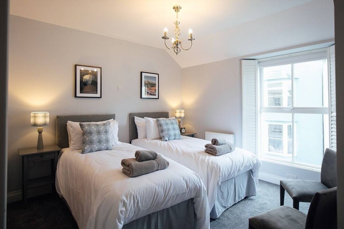 Une chambre d’hôtel avec deux lits, un lustre, des tableaux encadrés au mur et une fenêtre avec des stores.