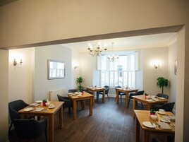 A dining area with wooden tables and chairs, a chandelier, and potted plants.