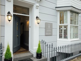 A building entrance with a dark blue door, two wall-mounted lanterns, a plaque, and a sign indicating vacancies.