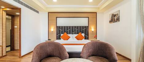 Una habitación de hotel con una cama grande, dos sillones, una mesita redonda y una mesita de noche.