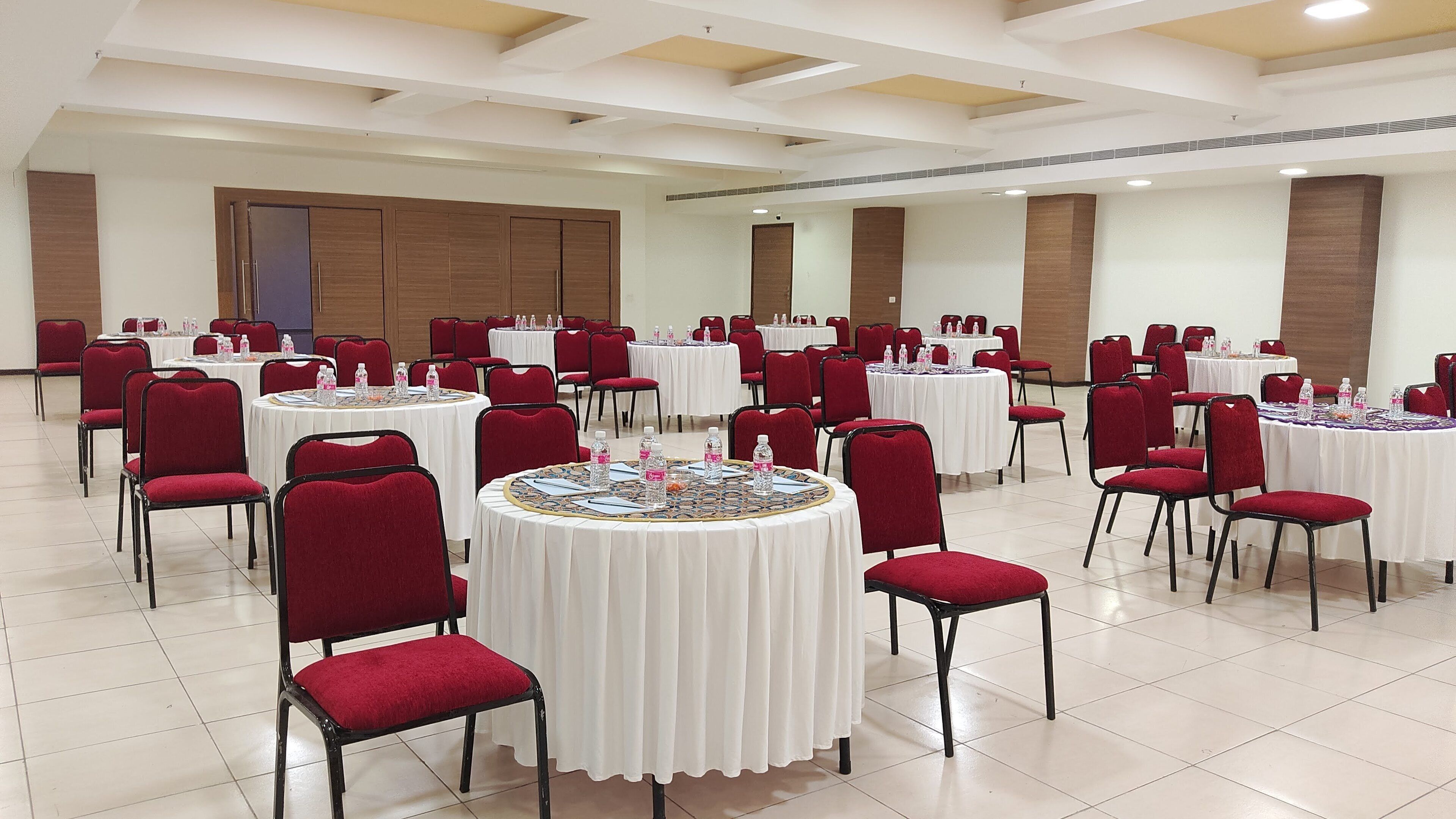 A conference room with round tables, red chairs, and white tablecloths.
