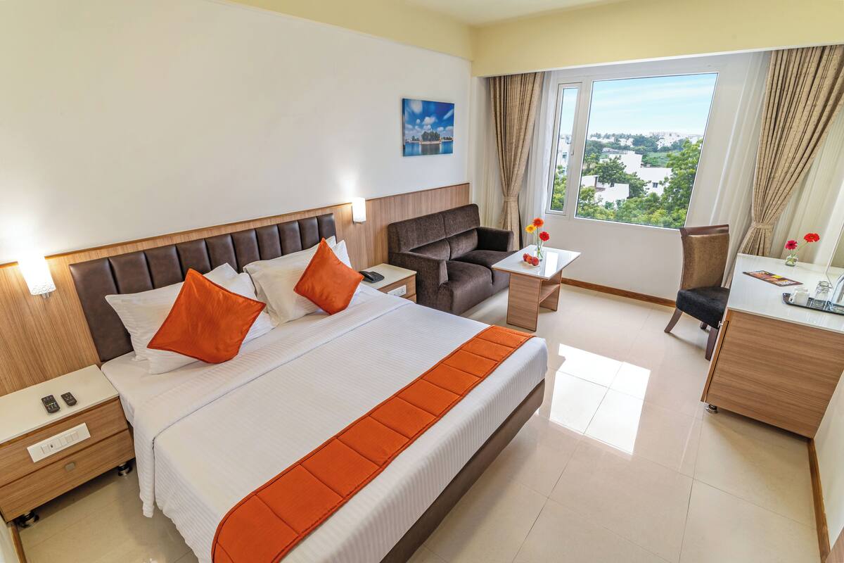 A hotel room with a large bed, a desk, a chair, and a view of the city.
