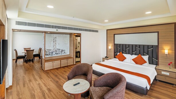 A hotel room with a bed, two armchairs, a small table, a desk with chairs, and a decorative wall panel. - Sterling V Grand Madurai (Madurai)